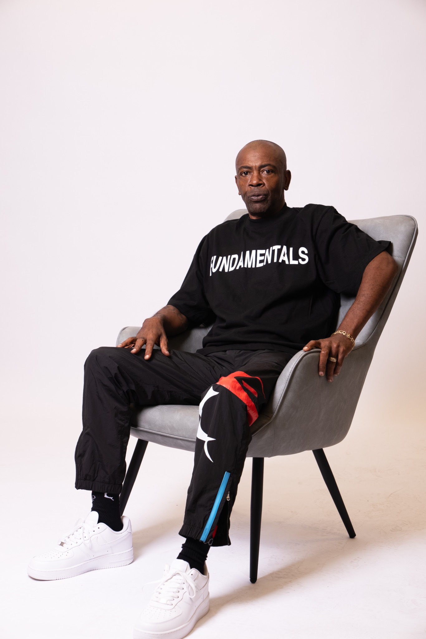 Seated model wearing a black Fundamentals T-shirt and Courtsmith track pants